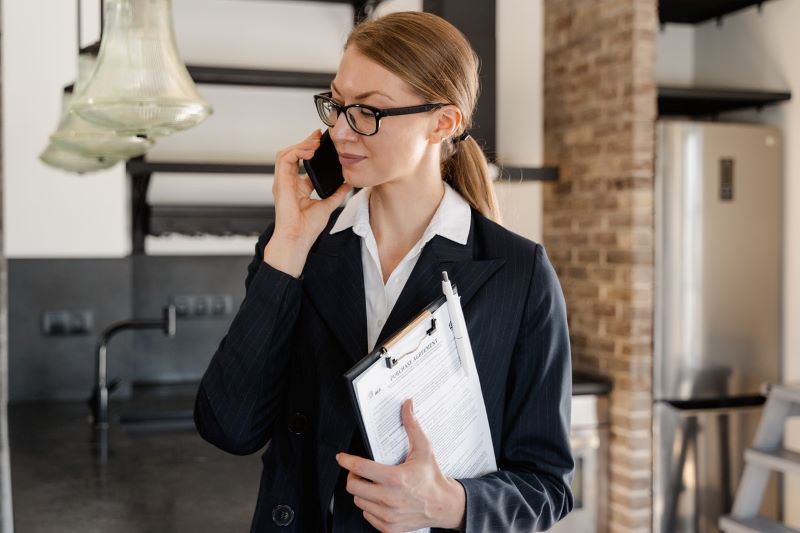 Female real estate agent on phone holding clipboard in kitchen of loft
