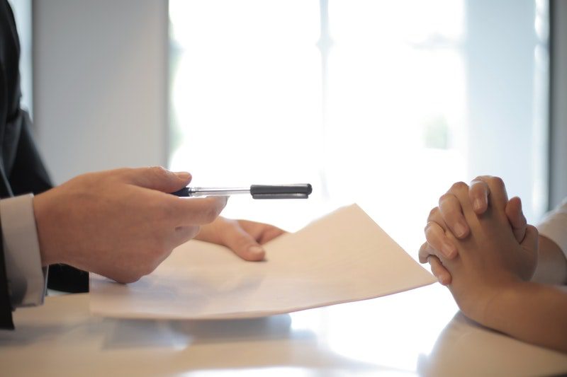 A closeup of a hand holding a pen and documents across from another set of hands