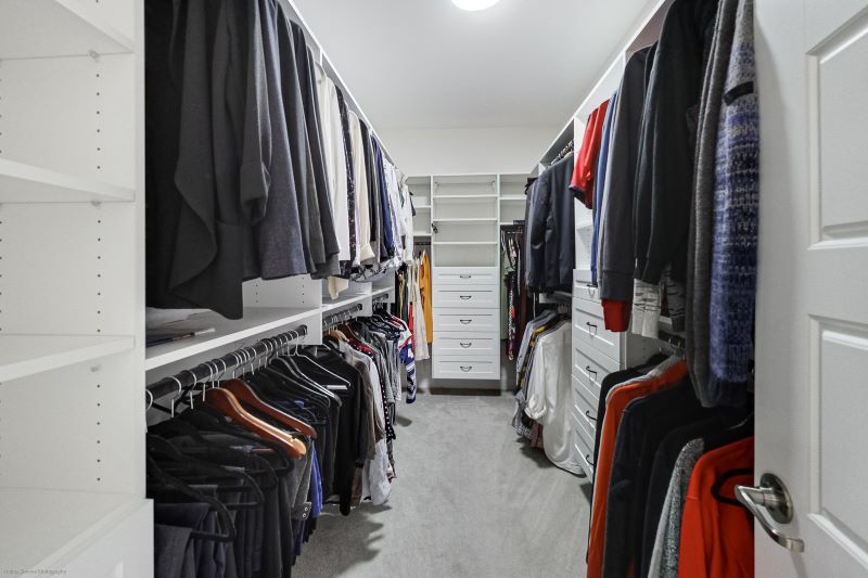 Large walk-in closet with white shelving units and clothing hung on upper and lower rods