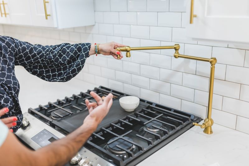 Close-up of female real estate agent turning on pot filler faucet above stovetop to show male home buyer